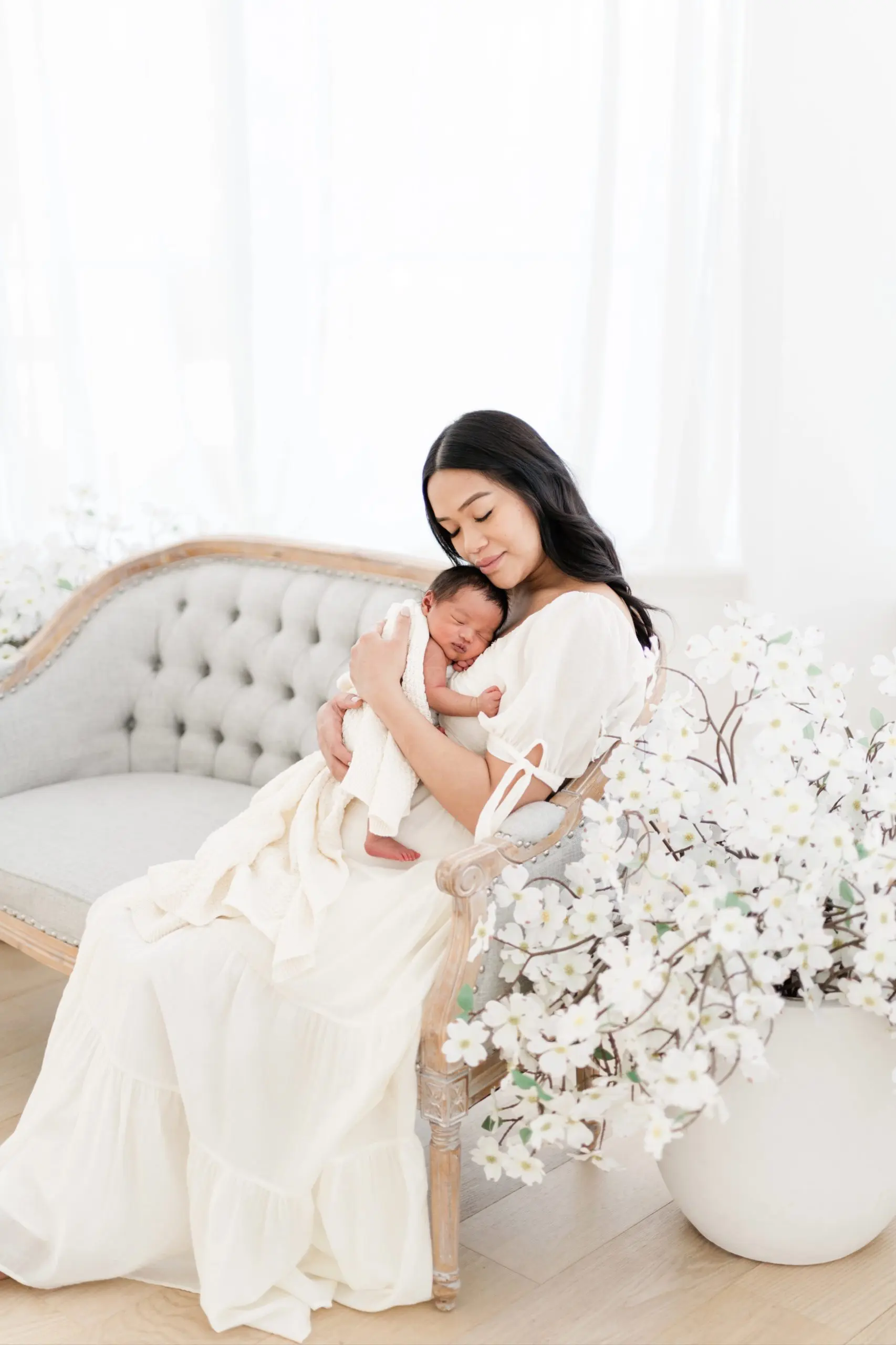 mother in white gown holding a sleeping swaddled newborn during a newborn photography session