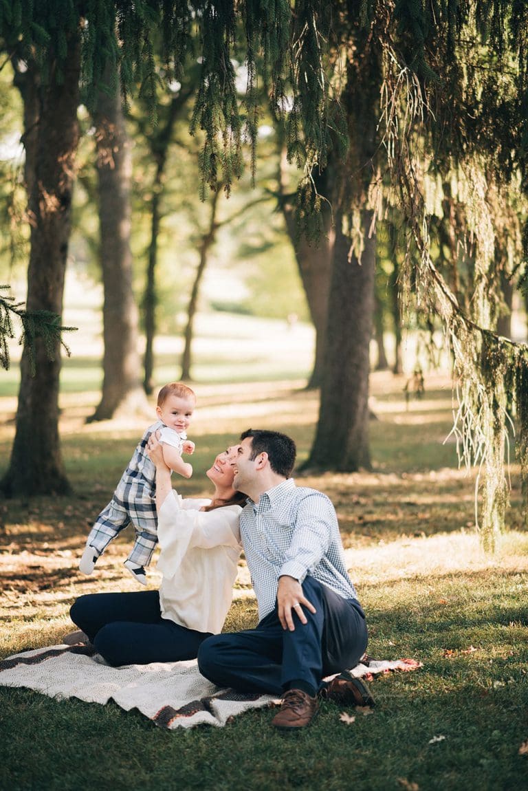 Family under tree holding up baby