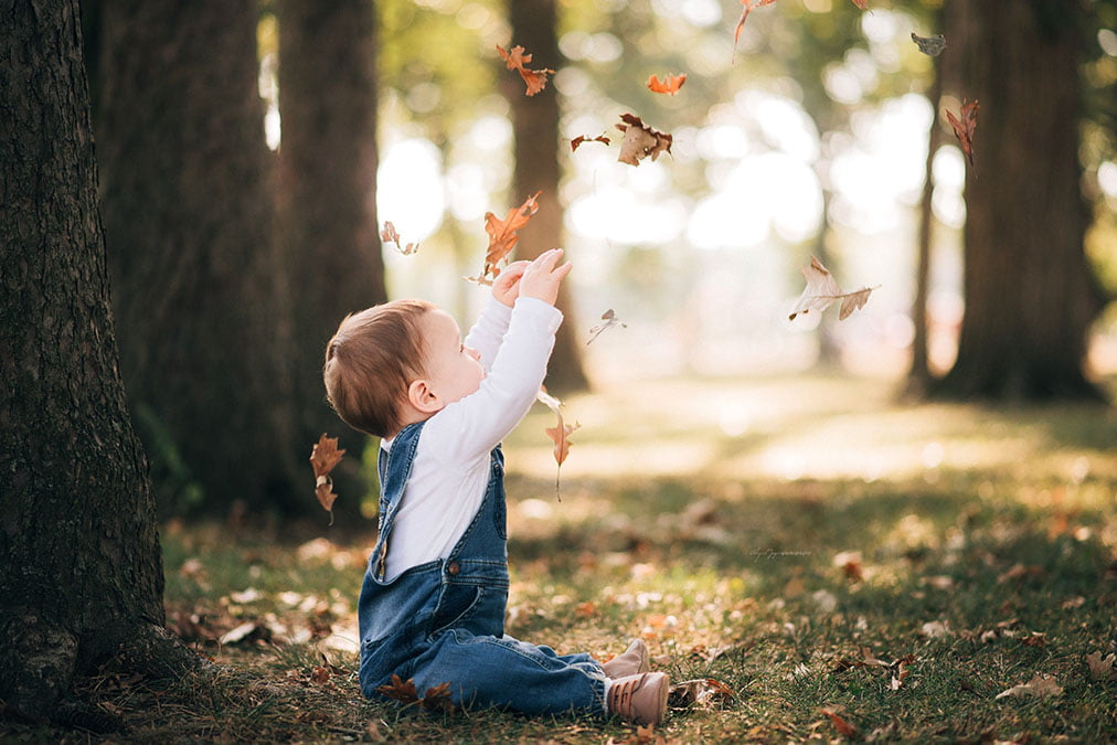 A baby boy throws leaves into the air during a portrait session