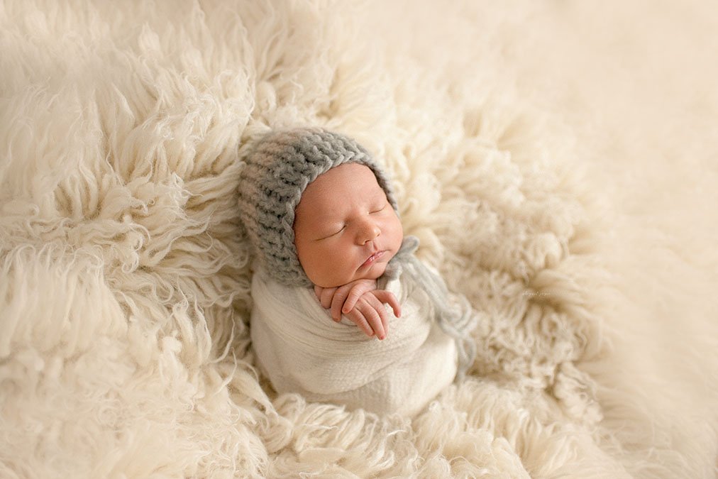 newborn baby swaddled and laying against a Flokati rug