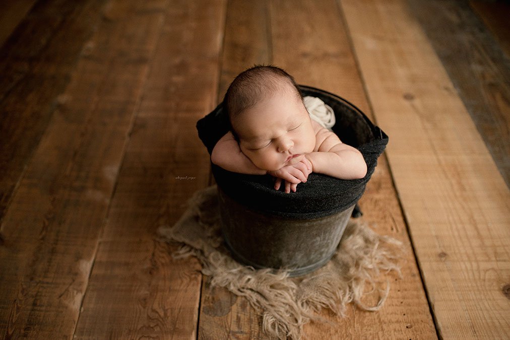 newborn laying in bucket on hardwood flooring