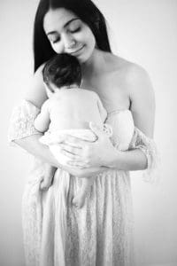 Mom holding baby girl against solid white wall