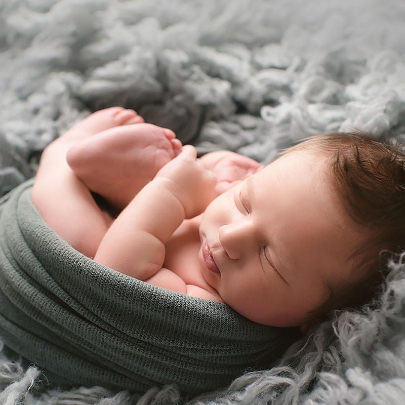 a baby lays swaddled in a dark grey flokati rug during an in-home newborn session in Oak Park, IL